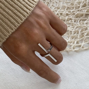 Minimalist silver asymmetric double-layer steel ring on hand with soft light close-up