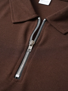 Detail of waffle knit fabric and silver zipper closure on a men's brown polo shirt