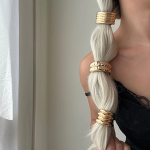 Detail of three golden metal hair rings including textured wide band and spiral ponytail cuffs