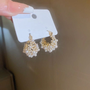 Close-up of gold-plated C-shaped earrings with multiple inlaid white pearls on card