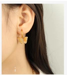 Detailed close-up of golden butterfly earrings with sparkling white zircons on ear