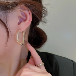 Macro detail of gold-plated twisted square earrings with pavé zircons on model ear