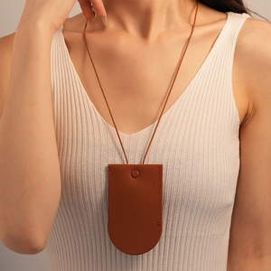 Close-up of a minimalist brown leather neck pouch on a white knitted top for women