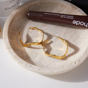 Golden wavy irregular hoop earrings on a stone tray with high-end aesthetic