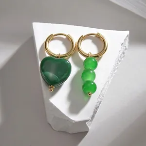 Détail de boucles d'oreilles dorées asymétriques avec pierre cœur et perles vertes