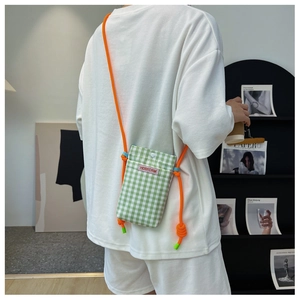 Detail of green checkered crossbody phone bag with orange rope strap shown on model back