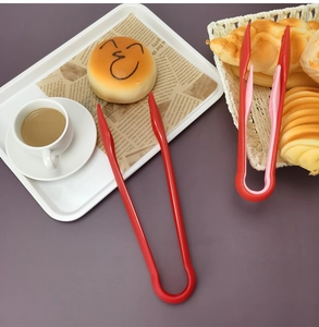 Flat lay of red and pink plastic food tongs set for baking and bread on a white tray