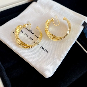 Detail of twisted multi-layer gold metal hoop earrings resting on a white drawstring pouch