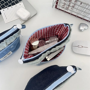 Detail of denim makeup bag with raw edges and red checkered lining on office desk
