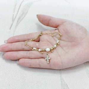 Detail of gold double-layered bracelet with cross pendant and pearls on palm