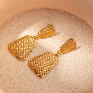 Boucles d'oreilles trapèze dorées avec texture tressée sur un plateau mat