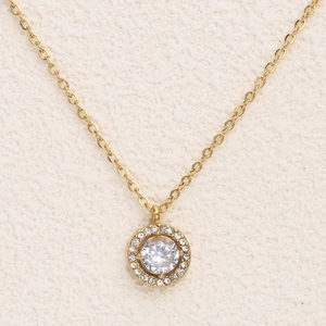 Collier en acier inoxydable plaqué or 18K avec pendentif rond pavé de cristaux sur fond beige