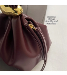 Detailed close-up of burgundy leather bag with smooth zipper and gold sculptural handle
