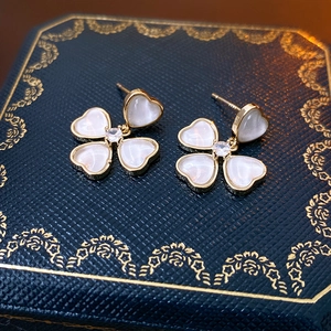Macro shot of gold clover earrings with white mother-of-pearl and heart detail