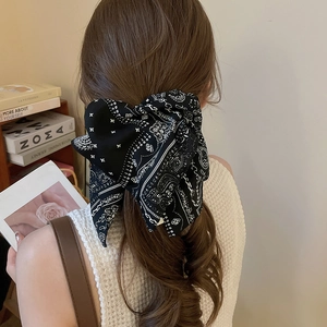 Détail d'un grand serre-tête en tissu à motif paisley noir et blanc porté par un modèle