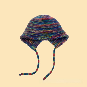 Detailed close-up of rainbow striped knit beanie with earflaps and braided tassel ties