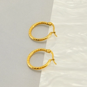 Detailed close-up of golden twisted hoop earrings on a marble surface background