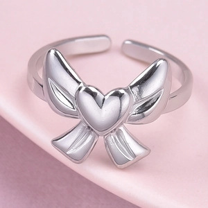 Détail d'un cœur argenté ailé sur une bague ajustable en acier inoxydable avec fond rose