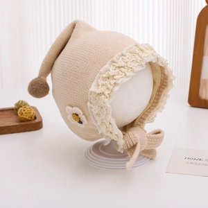 Detailed macro view of beige baby bonnet with delicate lace trim and embroidered flower