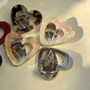 Detail view of heart-shaped acetate hair clip with gold logo and sturdy metal spring clip