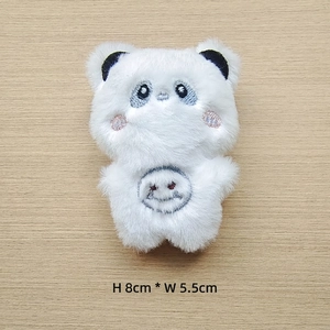 Detail view of 8x5.5cm white plush panda accessory with embroidery on wooden background