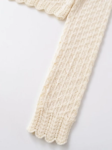 Close-up of cream white crochet knit top with intricate wavy patterns and scalloped edges