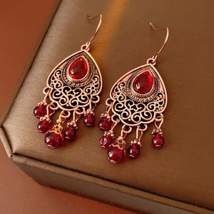 Dettaglio macro di orecchini vintage bohémien con motivi in bronzo e pietre rosse lucide