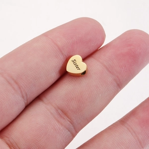 Macro shot of gold heart-shaped bead charm with Sister engraving held by hand