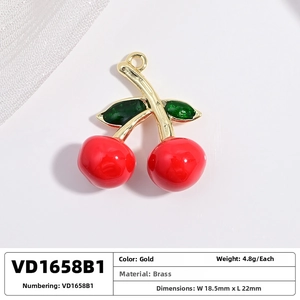 Detail view of a red cherry pendant crafted from brass with polished gold-tone leaf accents
