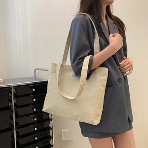 Detail of cream corduroy tote bag showing striped texture and blue fashion label