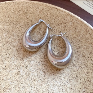 Detailed view of glossy silver teardrop-shaped metal hoop earrings on a textured ceramic tray