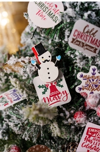 Close-up of Christmas wooden clips and tags on snowy tree with warm light bokeh