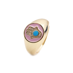 Golden Hamsa hand ring with pink enamel and blue gemstone inlay on white background