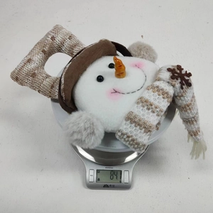 Detail view of a plush snowman doll showing fabric texture and weight of 84 grams