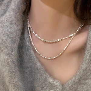 Gros plan de colliers argentés superposés à perles facettées sur un pull gris élégant