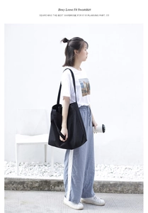 Detail of a large black canvas tote bag shown in a minimalist outdoor street setting