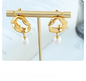 Detailed shot of gold-plated irregular lava earrings with white pearl pendants on stand