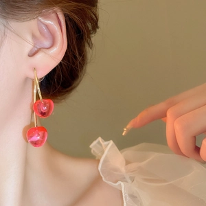 Detail of red cherry earrings with gold stems worn against a white ruffled collar