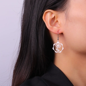 Detailed close-up of a model wearing a delicate hollow flower pendant earring in silver finish
