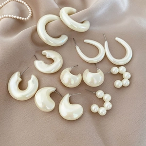 Detail view of pearl acrylic earrings and hoops set on beige silk backdrop