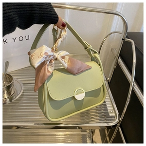 Detail of light green leather crossbody bag featuring gold buckle and floral silk scarf handle