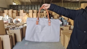 Détail du sac de voyage gris avec poignées brunes et poche de rangement avant