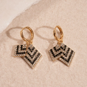 Detailed view of gold rhombus earrings with black and white rhinestones on stone background