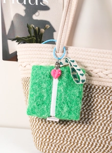 Green plush heart purse accessory with pink charm shown on a beige tote bag
