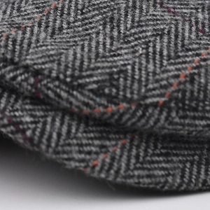 Close-up of charcoal herringbone tweed fabric with decorative orange stitching details