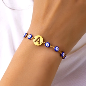 Macro detail of gold evil eye bracelet featuring an engraved letter A charm and blue beads