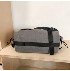 Side view of gray canvas cylinder duffel bag with black straps on a wooden stand