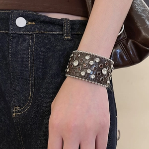 Gros plan d'un large bracelet en cuir avec des strass clairs et ambrés et des clous