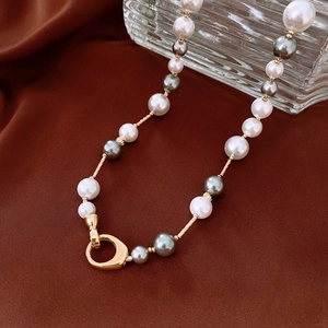 Détail d'un collier de perles blanches et grises avec un fermoir à bascule en or poli