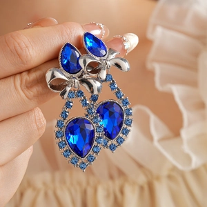 Macro shot of silver bow earrings featuring blue teardrop rhinestones held by hand